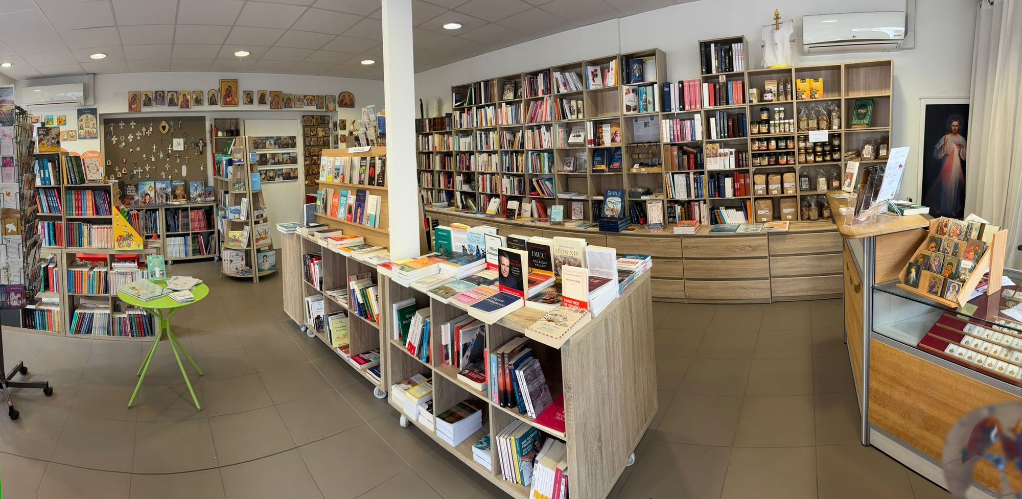 Vue d’ensemble de la librairie : rayonnages de livres, mur d’icônes, coin enfants et comptoir