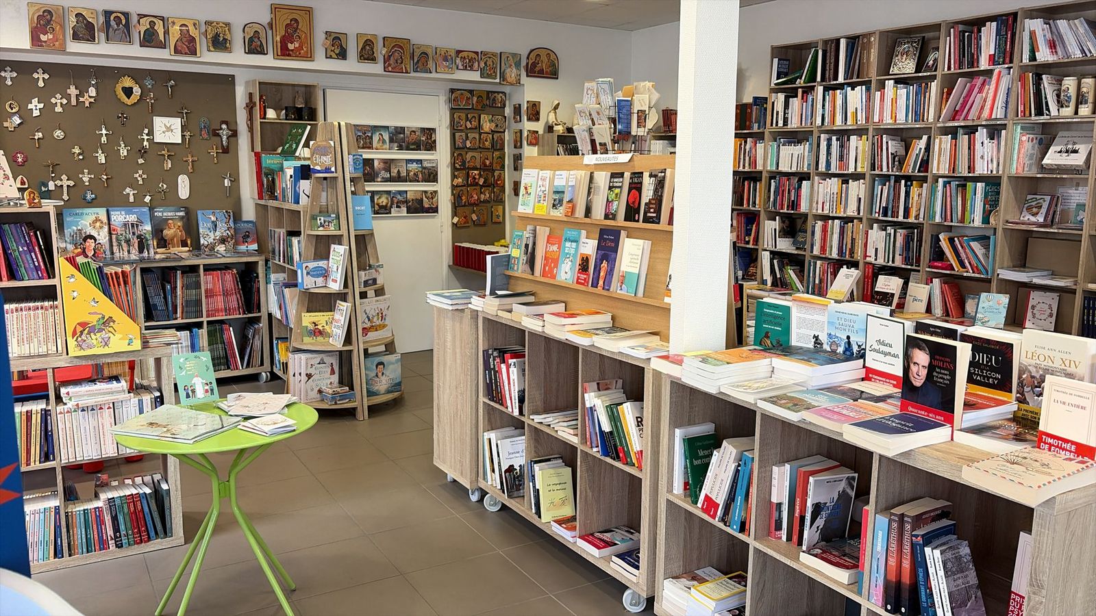 Intérieur de la librairie : mur d’icônes et de croix, présentoir des nouveautés, rayonnages